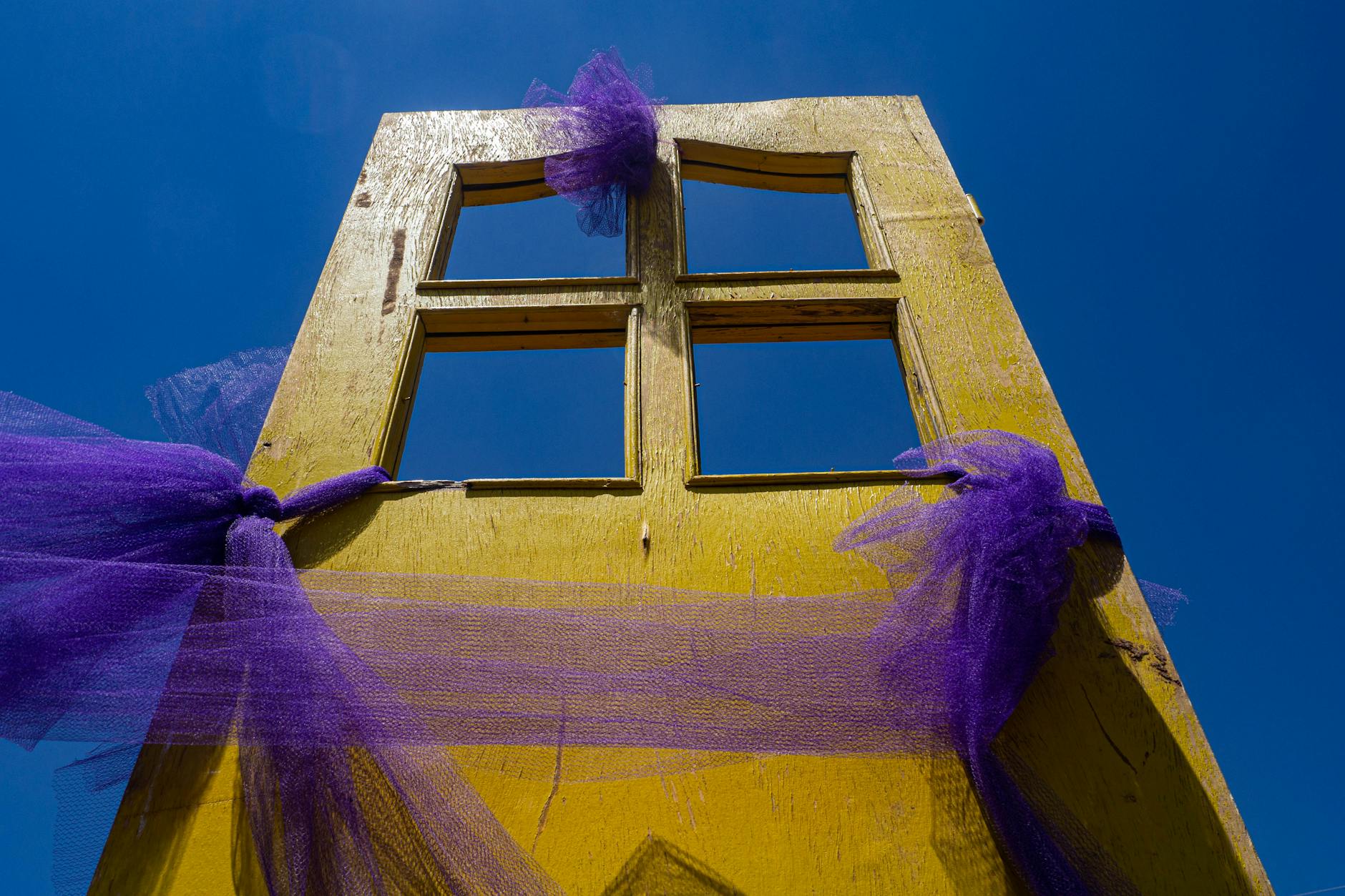 Żółte drzwi z fioletową siatką na tle błękitnego nieba