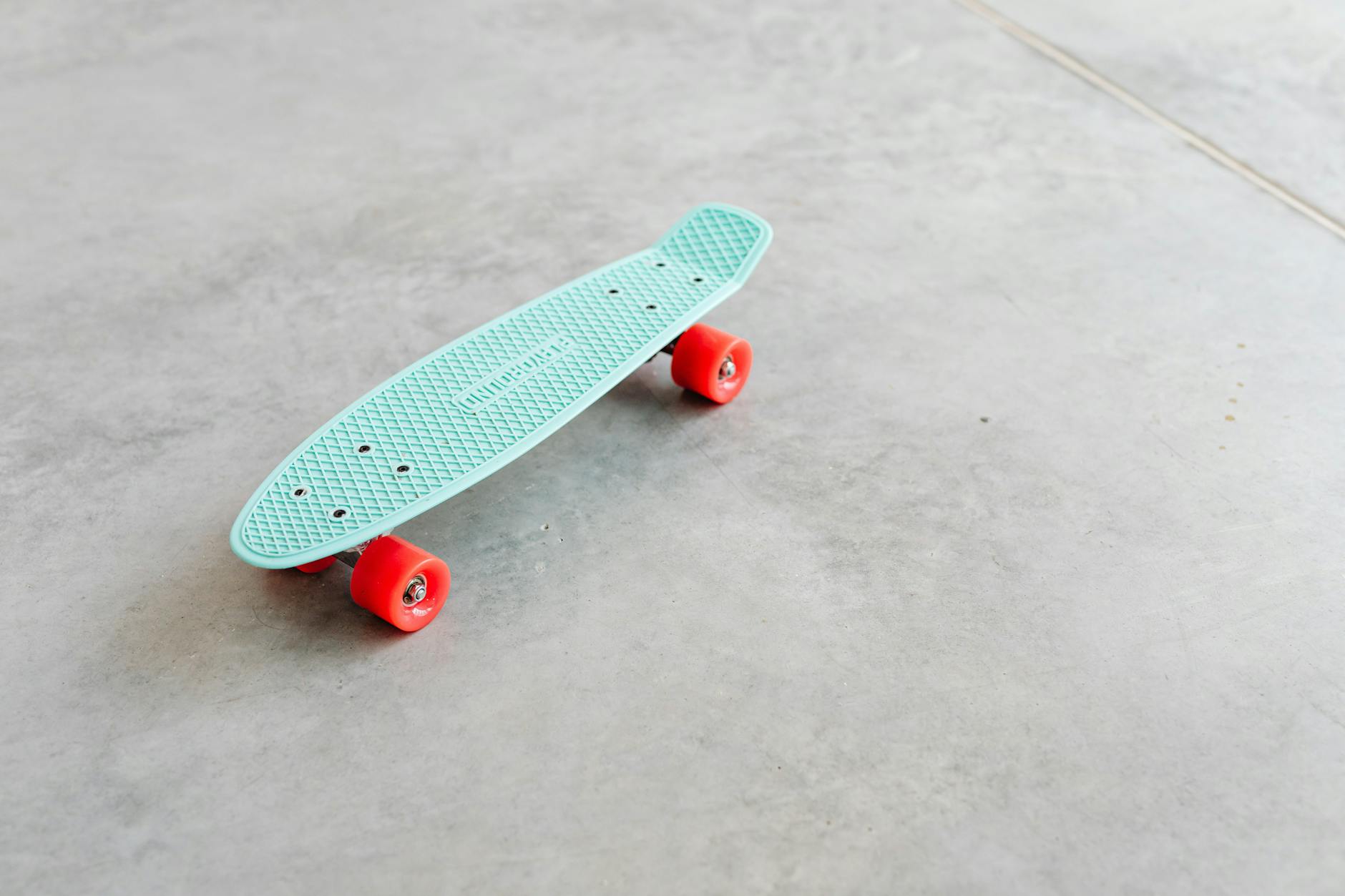 Błękitna deskorolka typu penny board z czerwonymi kółkami na betonie