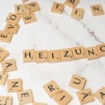 Jak prefabrykowane ściany drewniane poprawiają szczelność i parametry cieplne? Kafelki scrabble układające się w słowo Heizung na marmurowym blacie