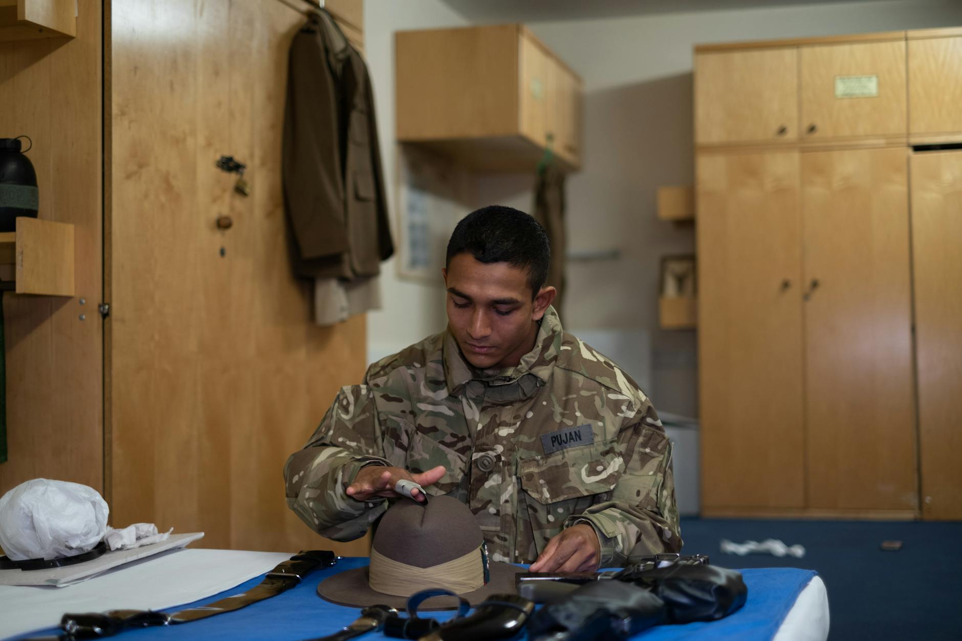 Żołnierz w baraku poleruje czapkę w wojskowej izbie