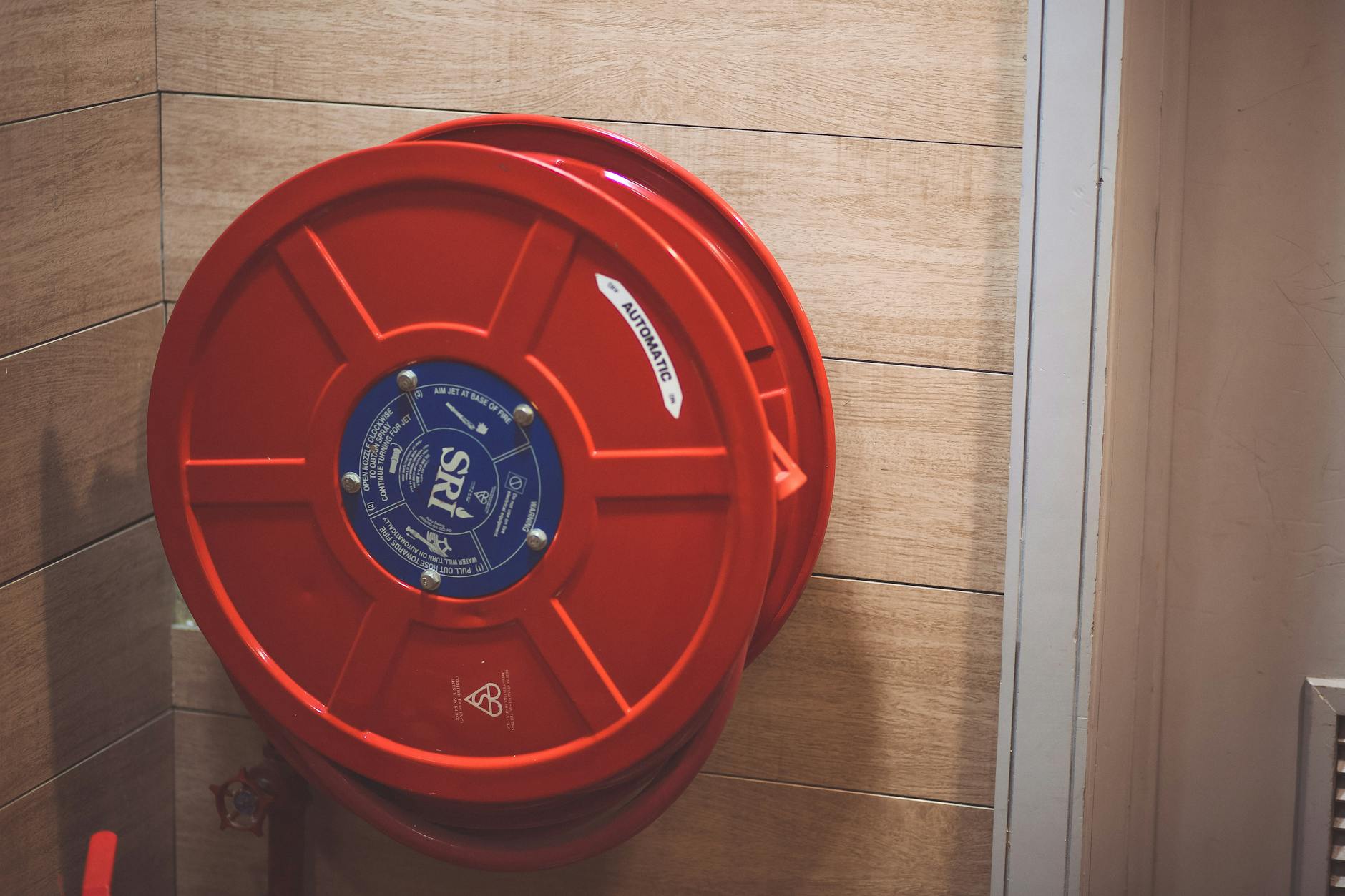 Drewno i ogień: jak zmieniały się przepisy i podejście do bezpieczeństwa pożarowego Czerwony bęben z wężem przeciwpożarowym na drewnianej ścianie