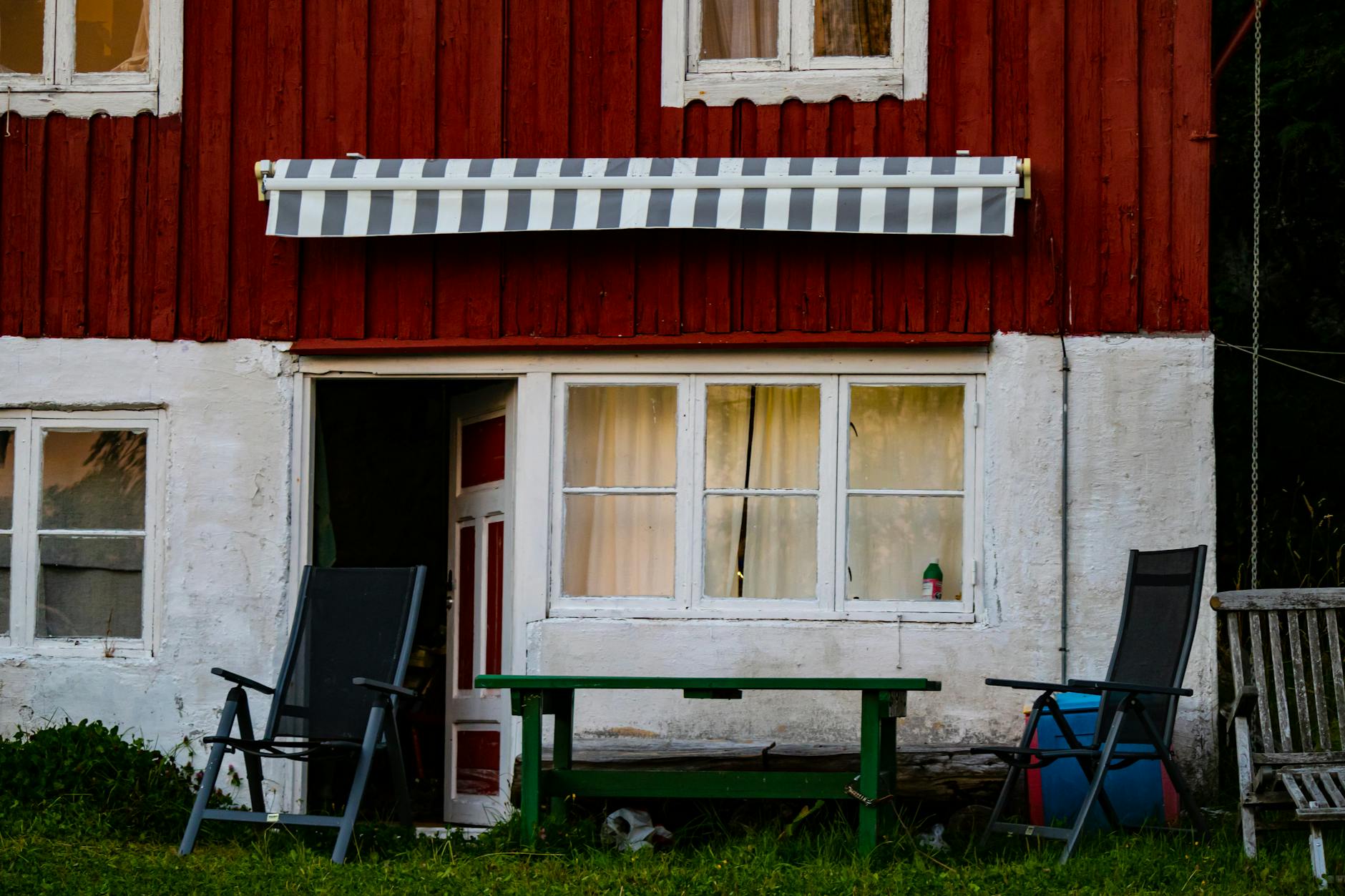 Drewniana rustykalna chata z czerwono-białą elewacją i miejscem do siedzenia