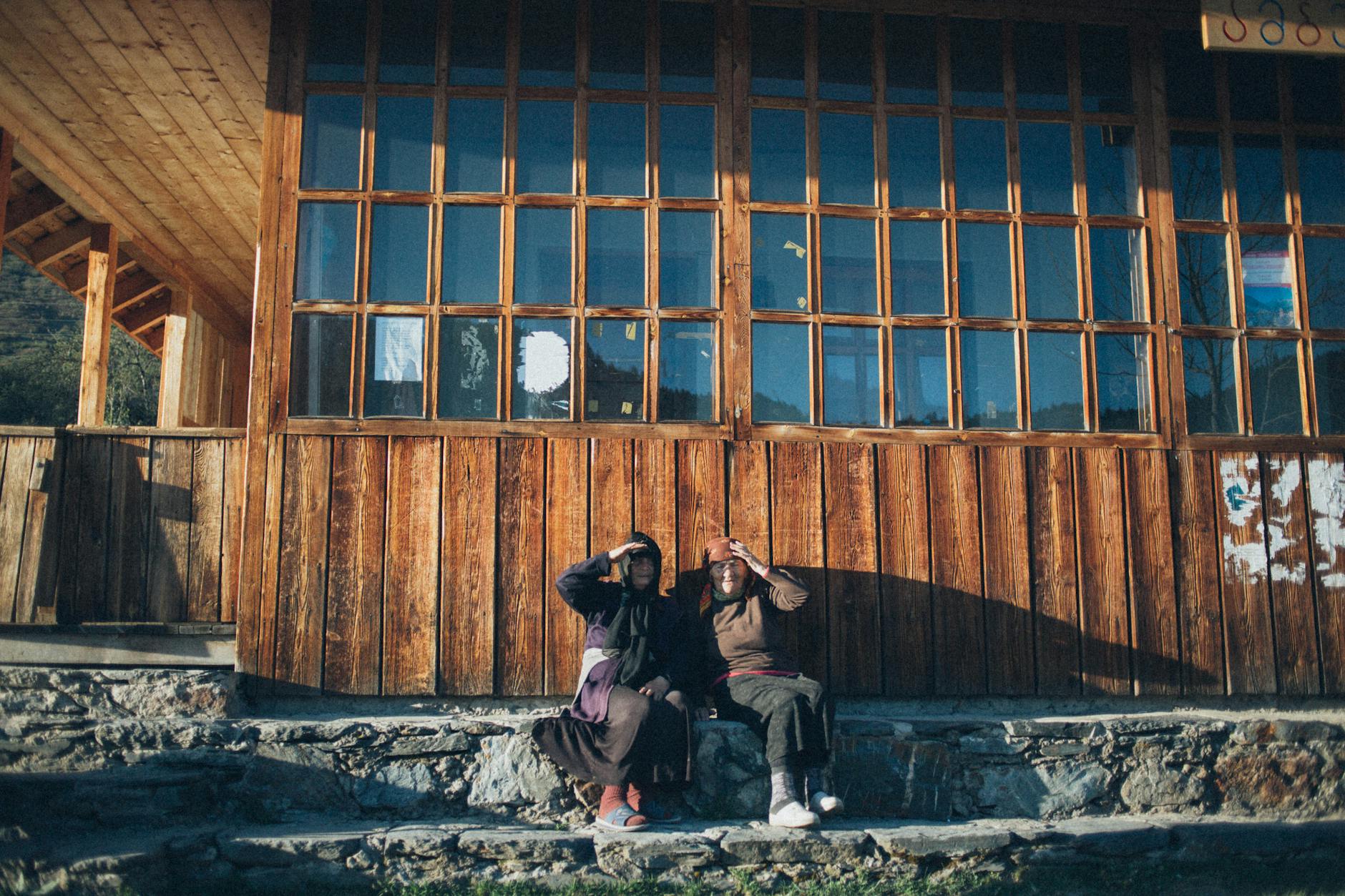 Dwoje starszych ludzi siedzi przy drewnianym domu w słoneczny dzień