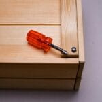 Najczęstsze błędy przy wkrętach do drewna i jak ich uniknąć Pomarańczowy wkrętak przykręcający wkręt w narożniku drewnianej skrzynki