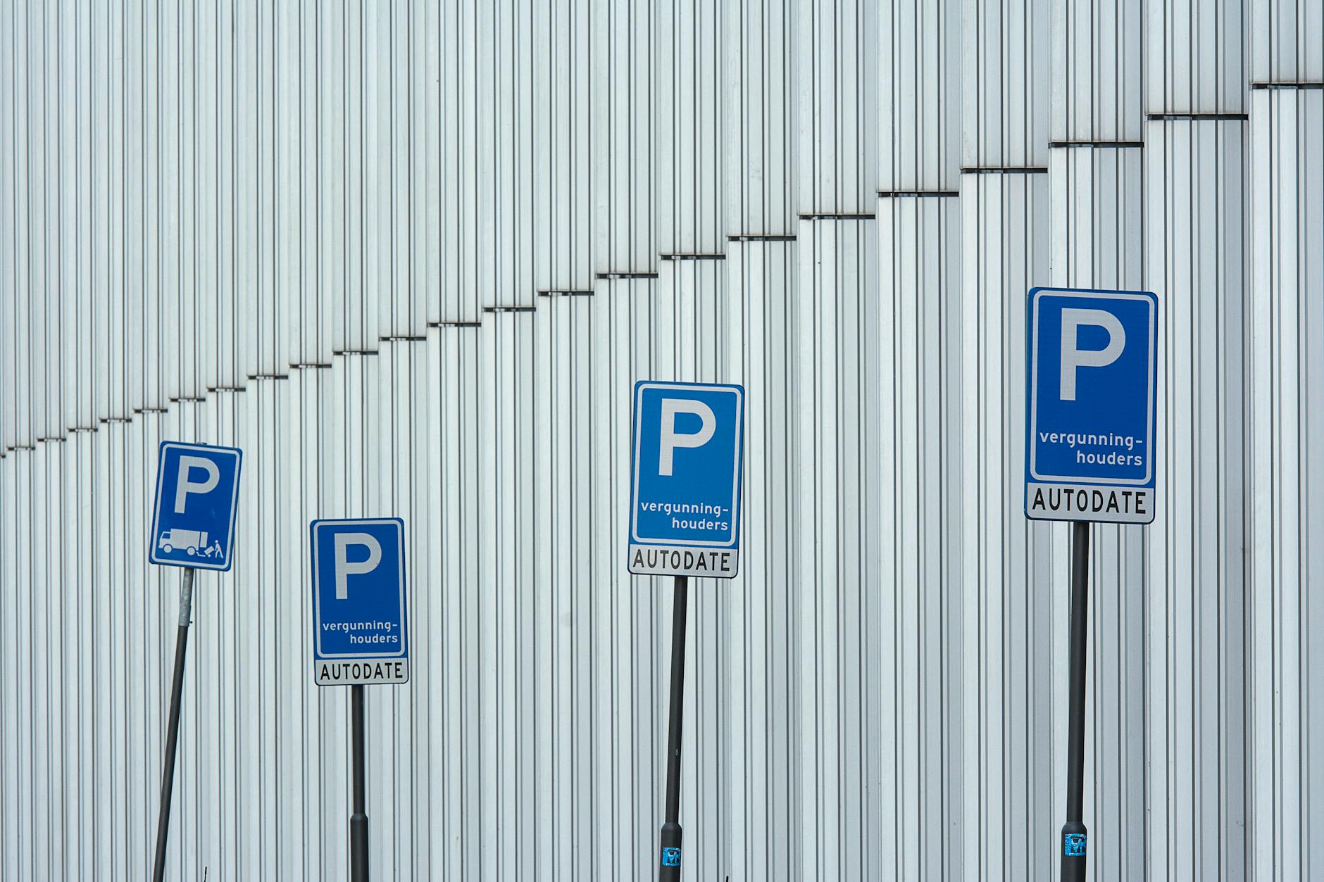 Rząd niebieskich znaków parkingu na tle nowoczesnej elewacji