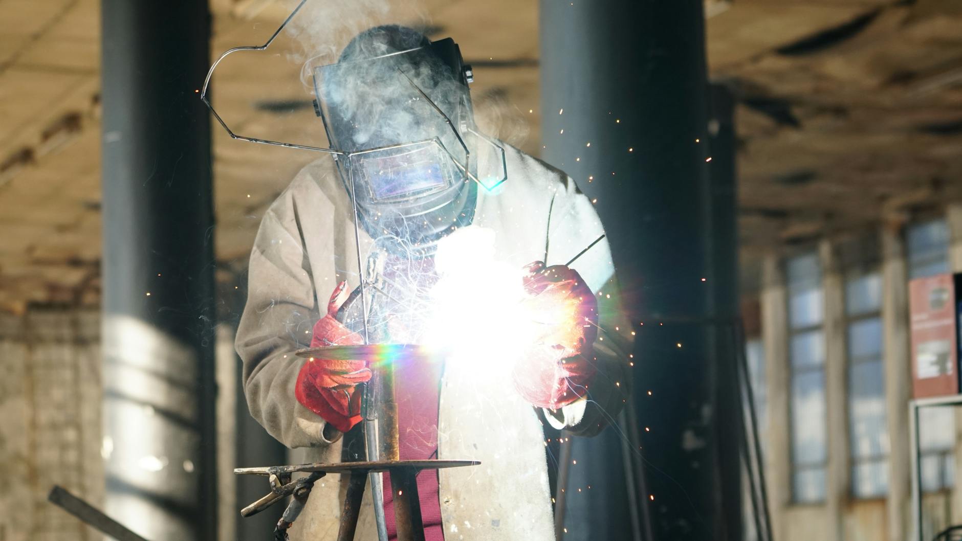 Spawacz w przyłbicy ochronnej podczas spawania metalu z iskrami