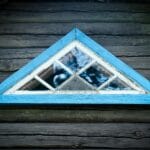 Czym różni się sosna, dąb i meranti w oknach? Trójkątne drewniane okno z niebieską ramą w rustykalnej ścianie