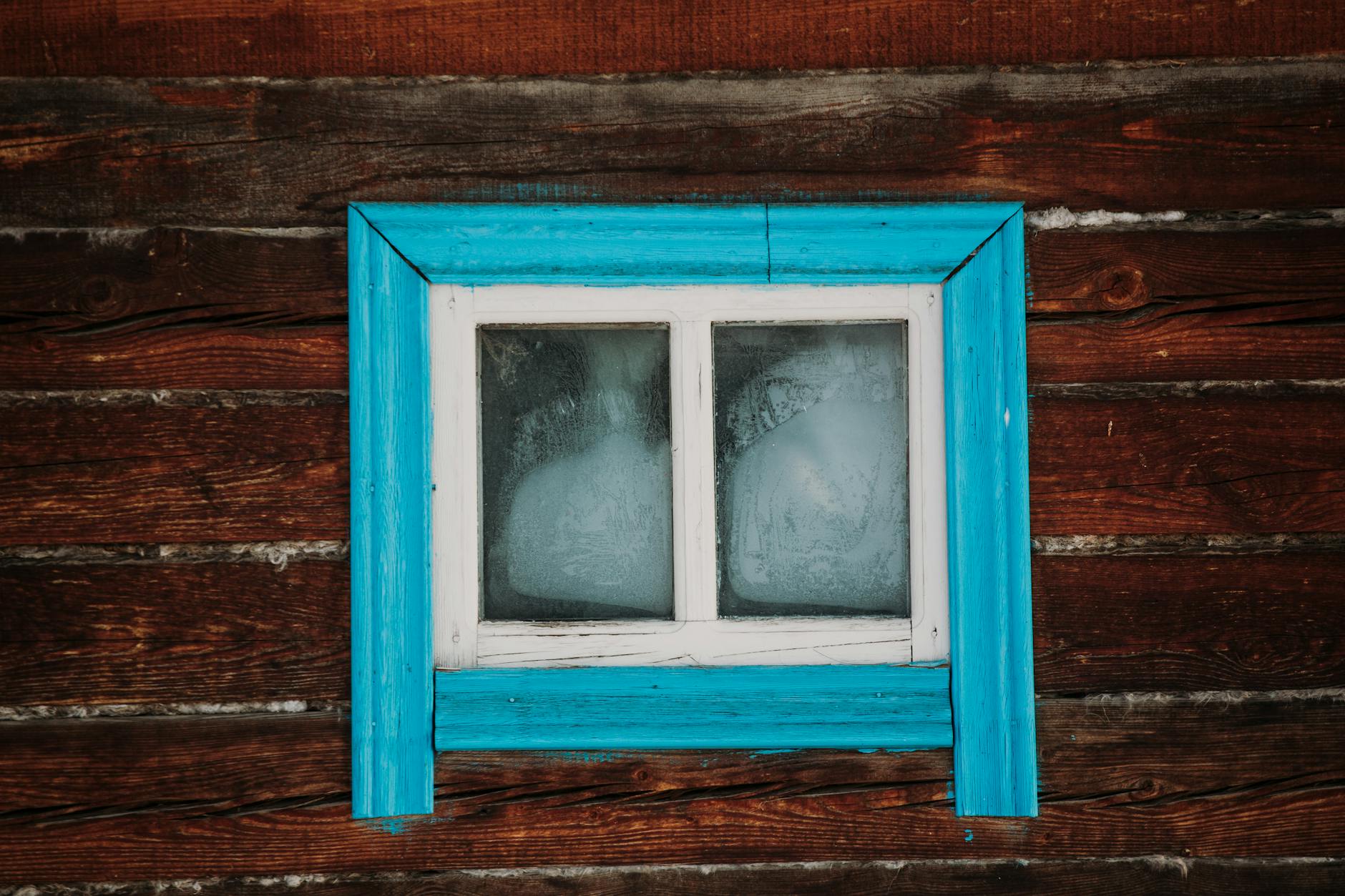 Zbliżenie starej drewnianej ściany z niebieskim oknem