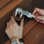 Dłonie mierzą drewniany element elektroniczną suwmiarką na stole