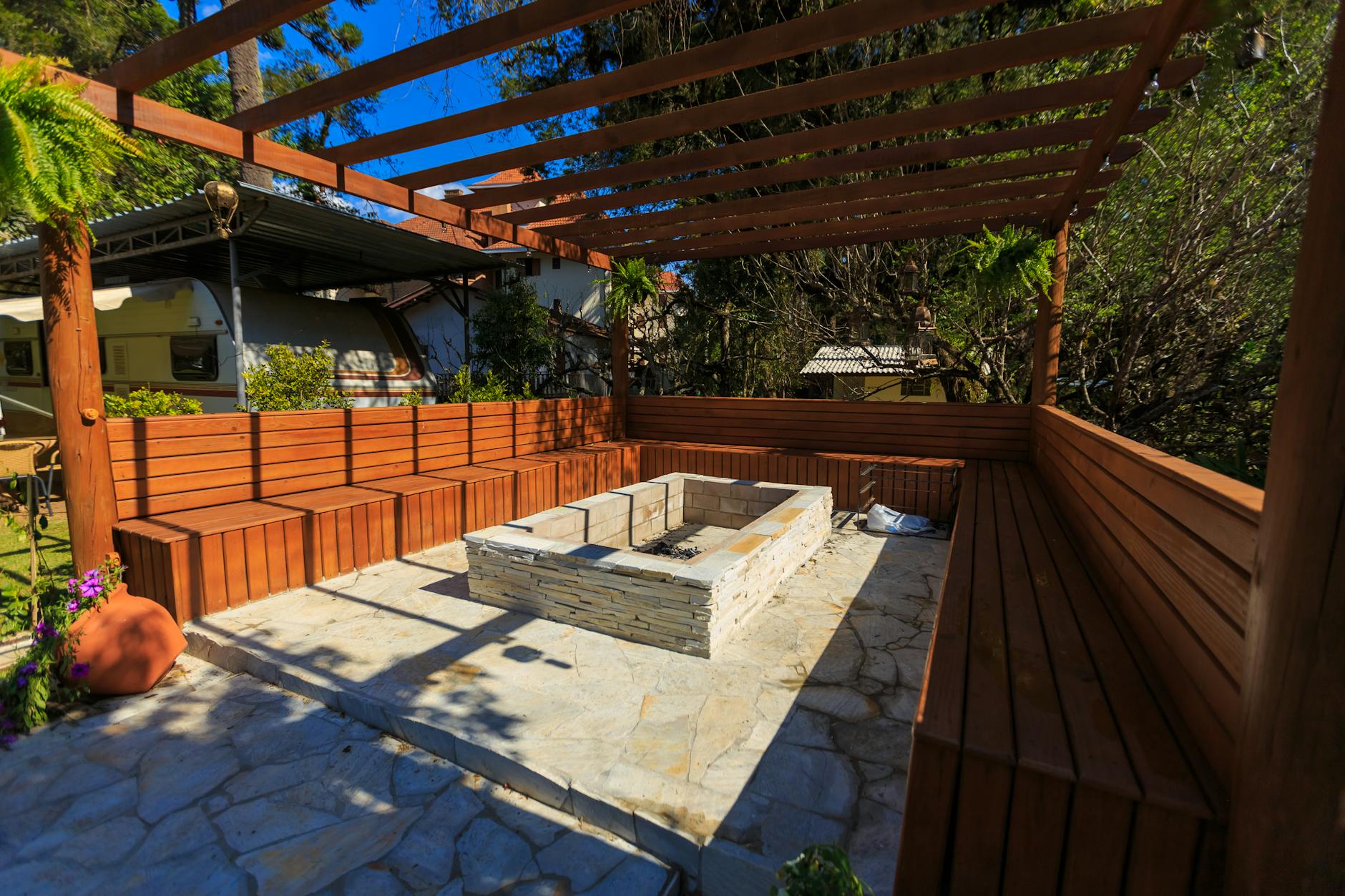 Drewniana pergola z ławkami i kamiennym paleniskiem na tarasie