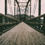 Jakie drewno wybierano do dawnych mostów i przepraw? Drewniany most wiszący nad rzeką z widocznymi detalami konstrukcji