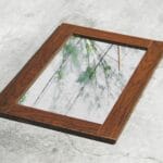 Lustro w drewnianej ramie leżące na betonie odbija drzewa i niebo