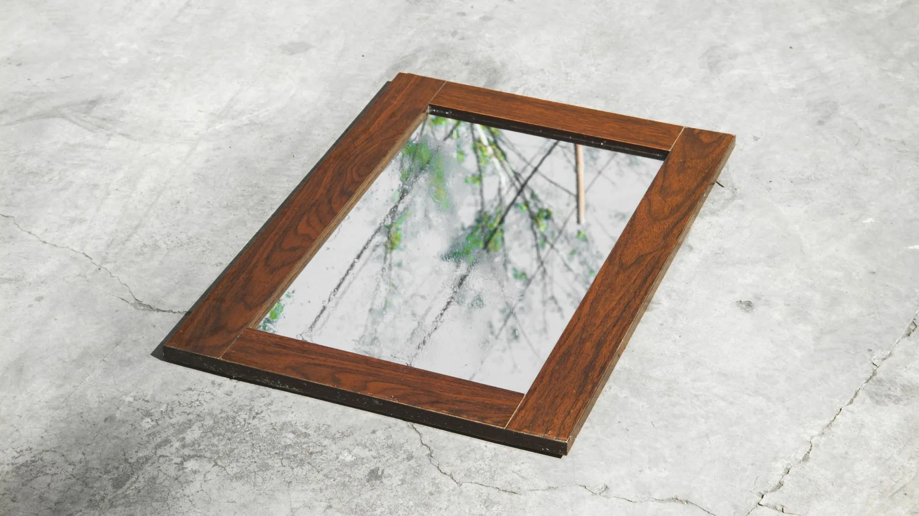 Jak zrobić ramę do lustra z drewna i ukryć mocowania, by wyglądała jak z pracowni stolarskiej Lustro w drewnianej ramie leżące na betonie odbija drzewa i niebo