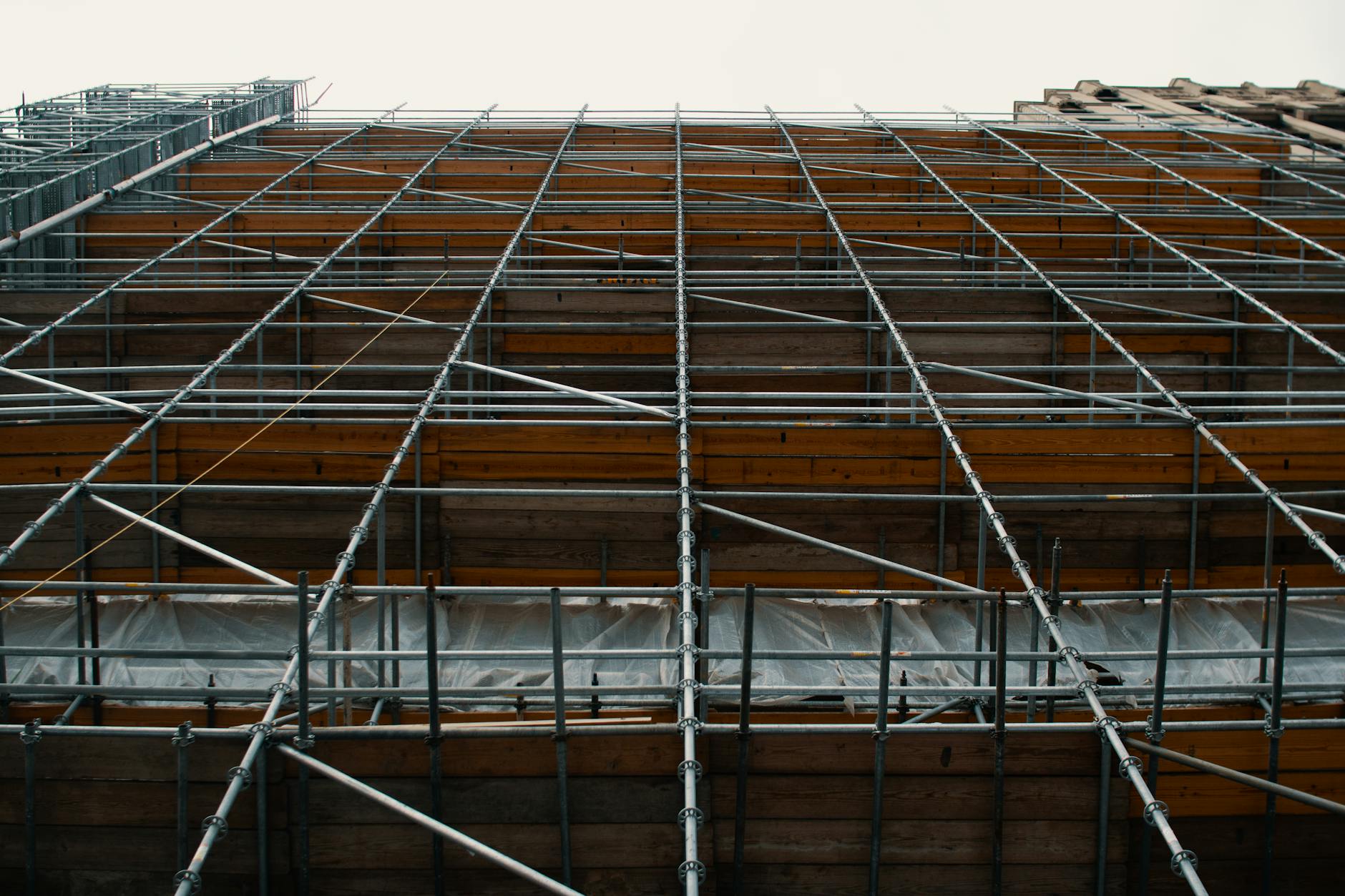 Jak wybrać deskę elewacyjną, żeby nie paczyła się po montażu? Rusztowanie przy elewacji budynku na tle zachmurzonego nieba