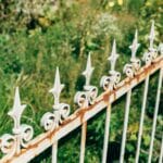 Czy opalanie drewna sprawdza się w ogrodzie? Trwałość i pułapki metody Zabytkowy, zardzewiały żeliwny płot na tle bujnego ogrodu