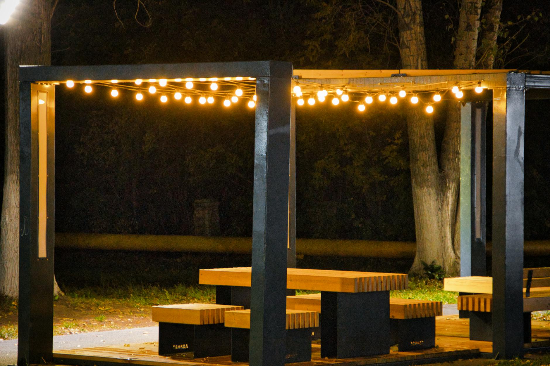 Krawędziaki na pergolę: jak wybrać proste i suche drewno z tartaku Drewniana altana w ogrodzie oświetlona ciepłymi girlandami wieczorem