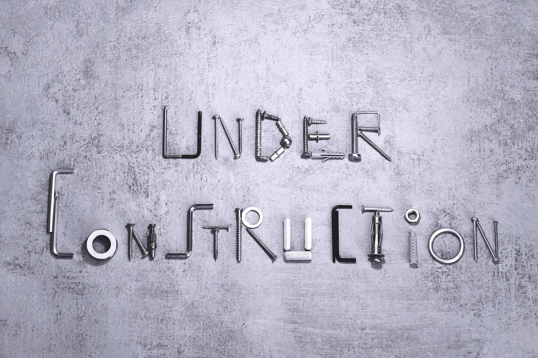 Czarny montaż w szkielecie: gwoździe czy wkręty konstrukcyjne, co daje lepszą wytrzymałość? Napis under construction ułożony z wkrętów i narzędzi na betonie