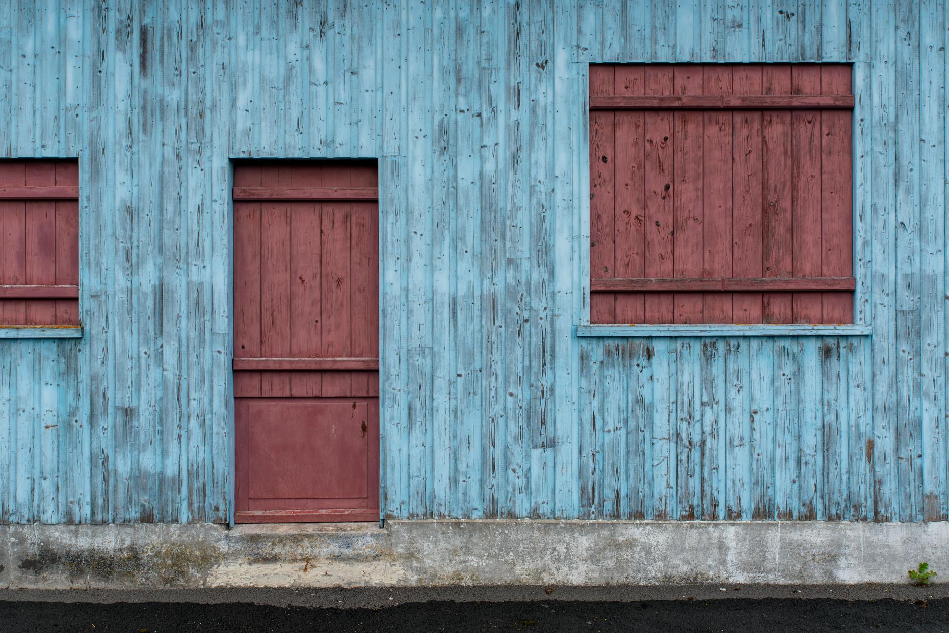 Naturalne starzenie drewna na elewacji: trend na patynę czy problem do opanowania Niebiesko-czerwona, postarzana drewniana elewacja o rustykalnej fakturze