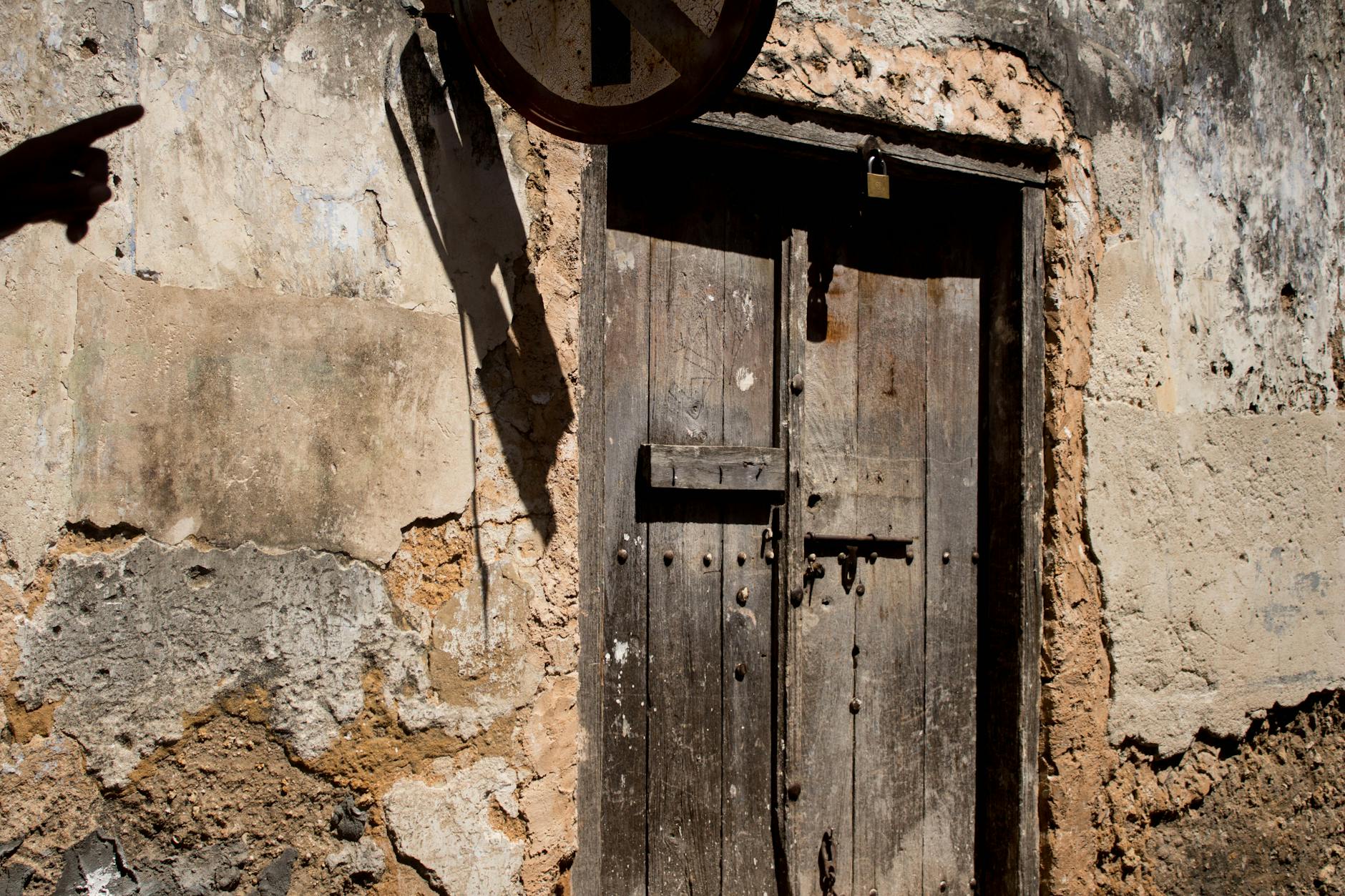 Stare drewniane drzwi w kamiennej ścianie w Zanzibarze, cień ludzkiej dłoni