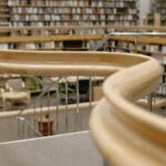 Drewniana, kręta poręcz i regały z książkami w bibliotece uniwersyteckiej