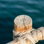 Zbliżenie drewnianego słupa pomostu z liną przy wodzie w marinie
